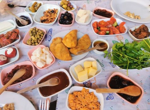 Ankara kahvaltı mekanları Ankara Ege usulü serpme kahvaltı mekanı Zeytuni Cafe’de sunulan, doğal ve yöresel ürünlerle zenginleştirilmiş, pişi ve peynir çeşitlerinin görüldüğü kalabalık kahvaltı masası.