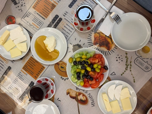 Eskişehir gezilecek yerler arasında olan doyuran kahvaltı salonunda masadaki peynir, zeytin, salatalık domates ve kaymak gibi kahvaltılıklar.
