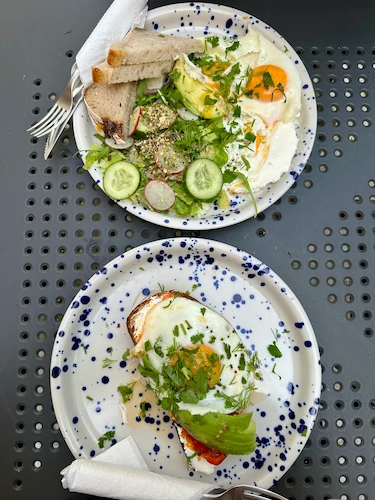 Wesoła Cafe'de ekmek üstü yumurtalı, avokadolu ve salatalı bir kahvaltı tabağı.